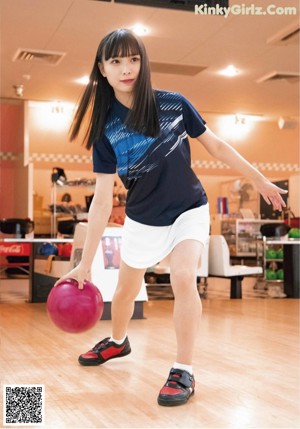 A woman in a red shirt and black skirt playing bowling.