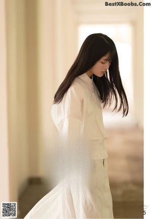 A woman with long black hair leaning against a fence.