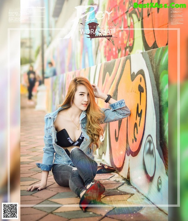 A woman sitting on the ground in front of a graffiti wall.