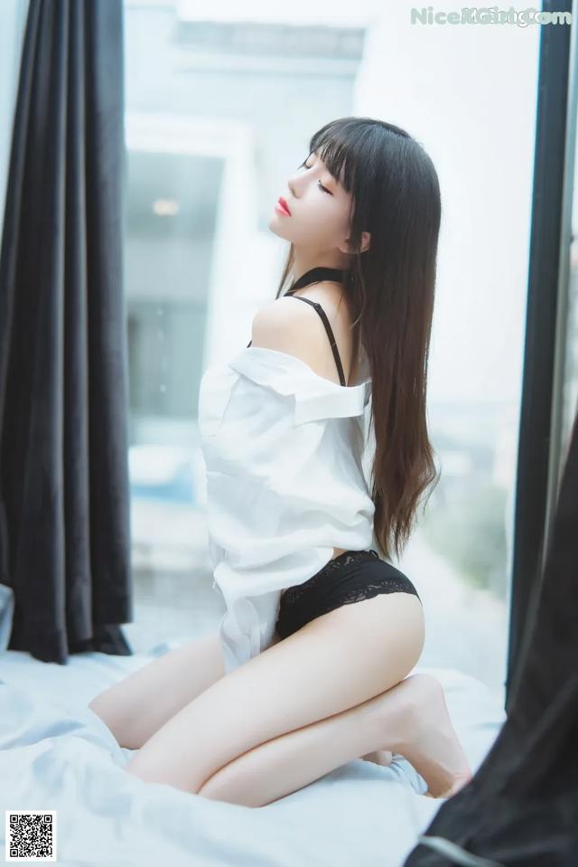 A woman sitting on a bed in a white shirt and black panties.