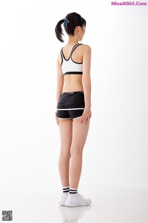 A woman in a sports bra top and shorts leaning against a wall.