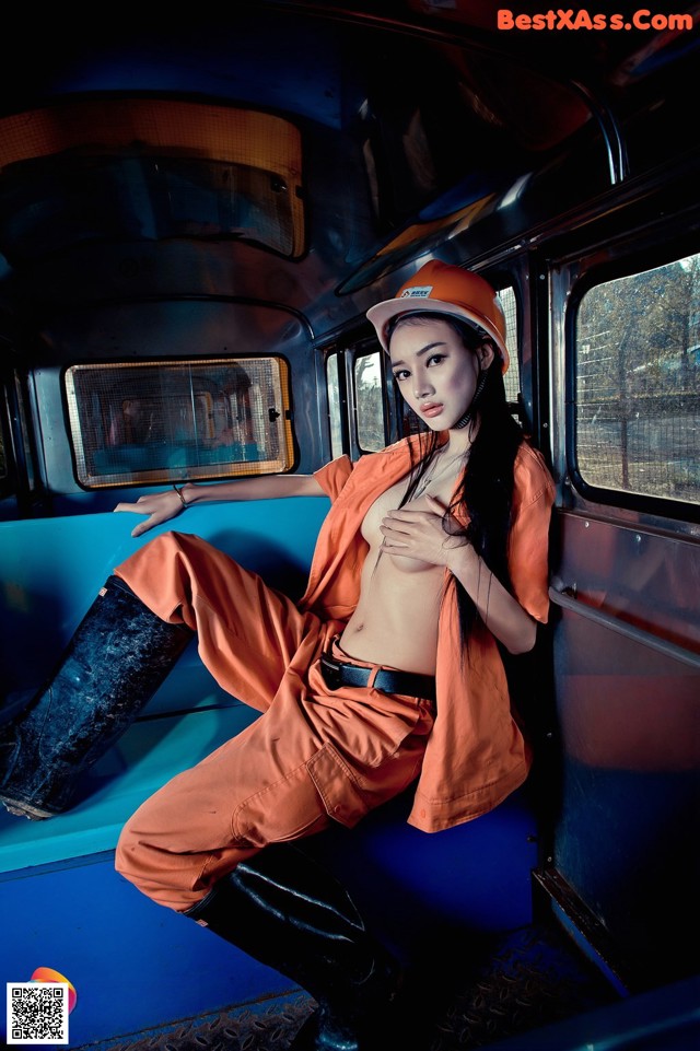 A woman in an orange jumpsuit sitting on a blue bus.