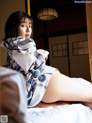 A woman in a blue and white kimono sitting on a bed.