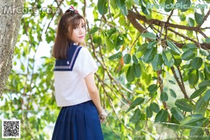 A woman in a school uniform standing in front of a tree.