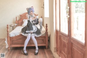 A woman in a maid outfit sitting on a bed.