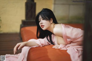 A woman in a pink dress sitting by a swimming pool.