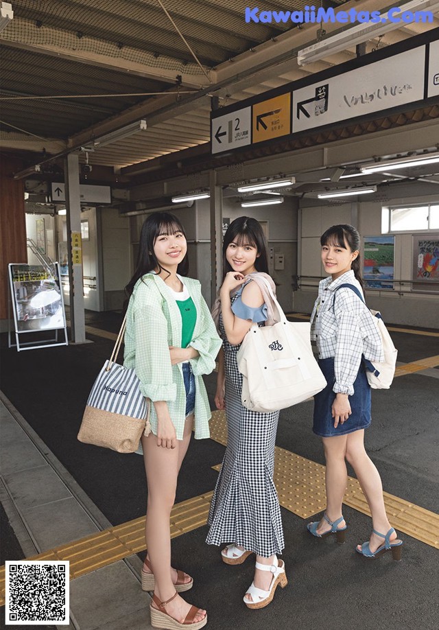 A group of three women standing next to each other at a train station.