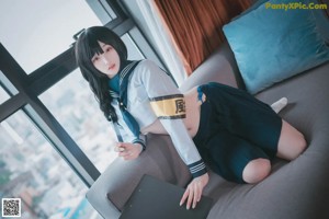 A woman in a school uniform sitting on a couch.