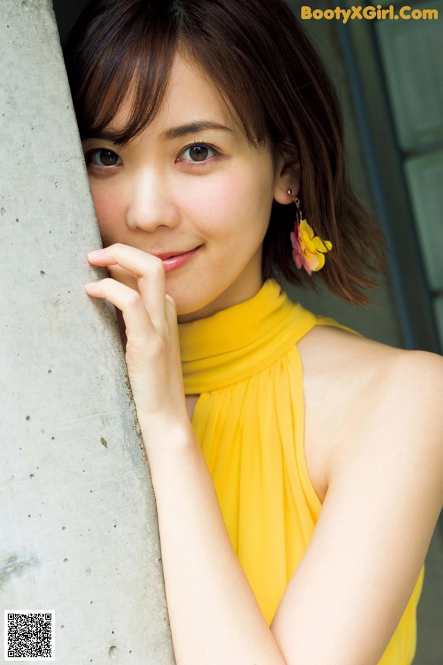 A woman in a yellow dress leaning against a wall.