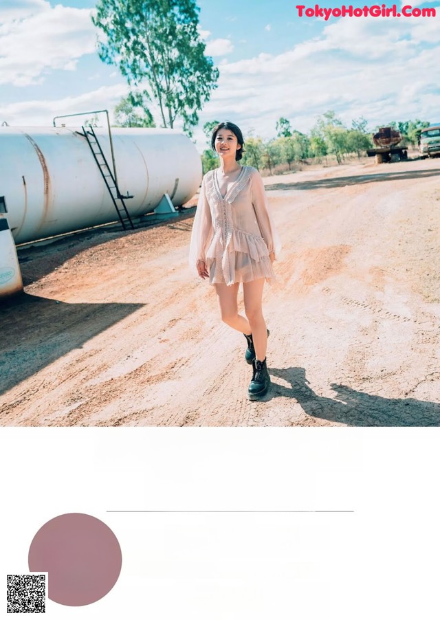 A woman walking down a dirt road next to a tank.