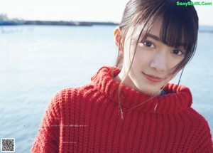 A woman in a red sweater is walking on the beach.