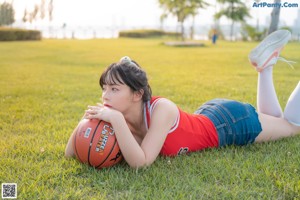A woman in a red shirt and denim shorts holding a basketball.