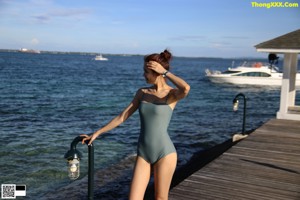 A woman in a white shirt and black bikini posing by a pool.