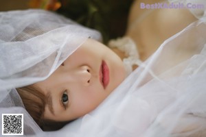 A woman laying on a bed covered in a veil.